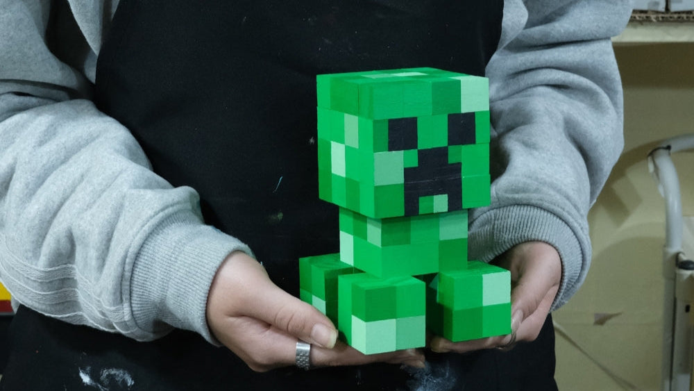 Handcrafted Minecraft Creeper wooden figure being held by artisan in grey sweater.