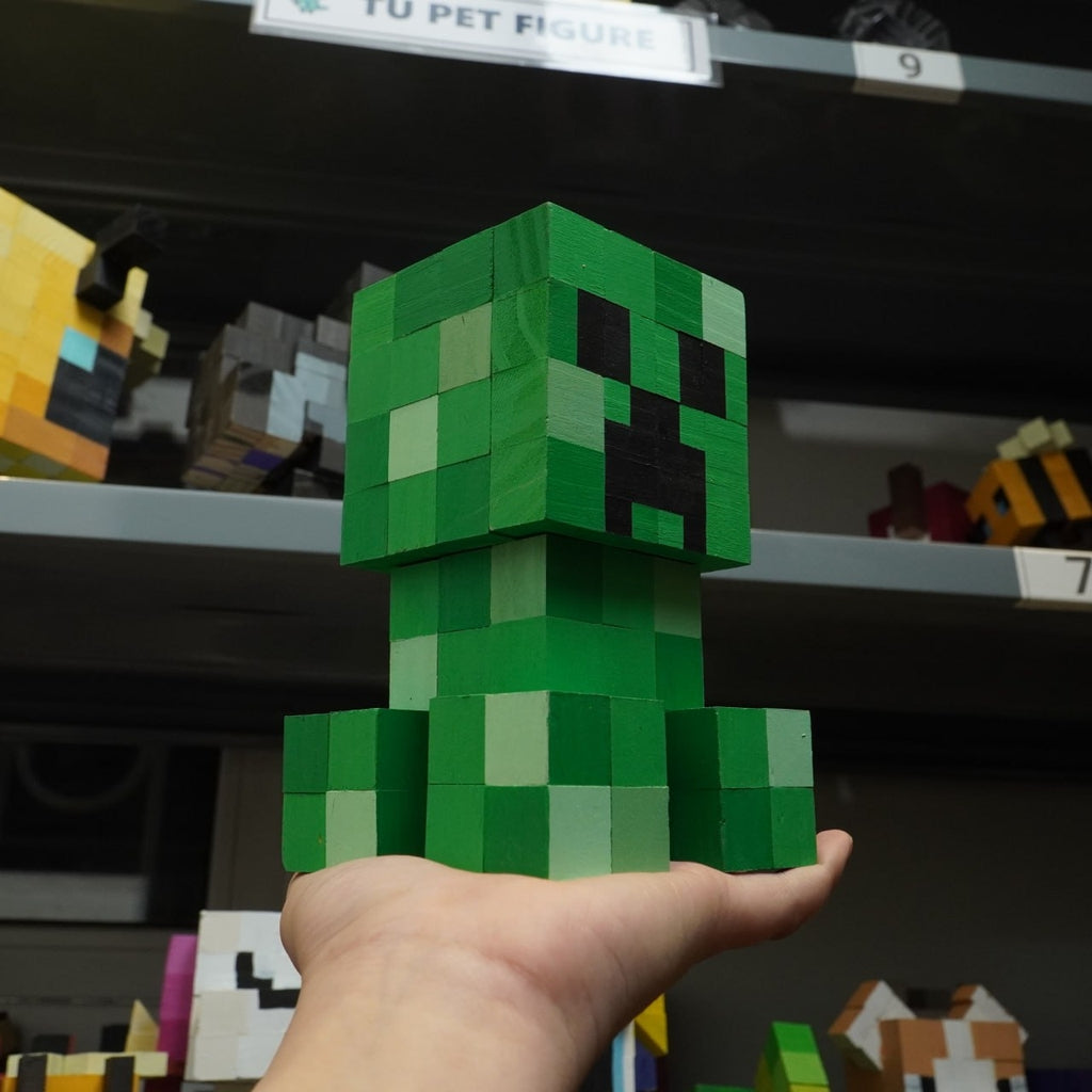 Wooden Minecraft Creeper model held in hand with pixel toy collection background.