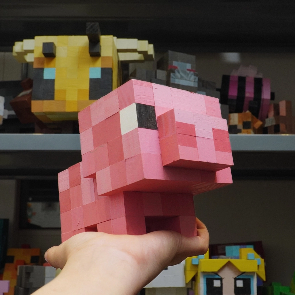 Handcrafted wooden Minecraft pig toy, pixel art style, showcased among other wooden models.