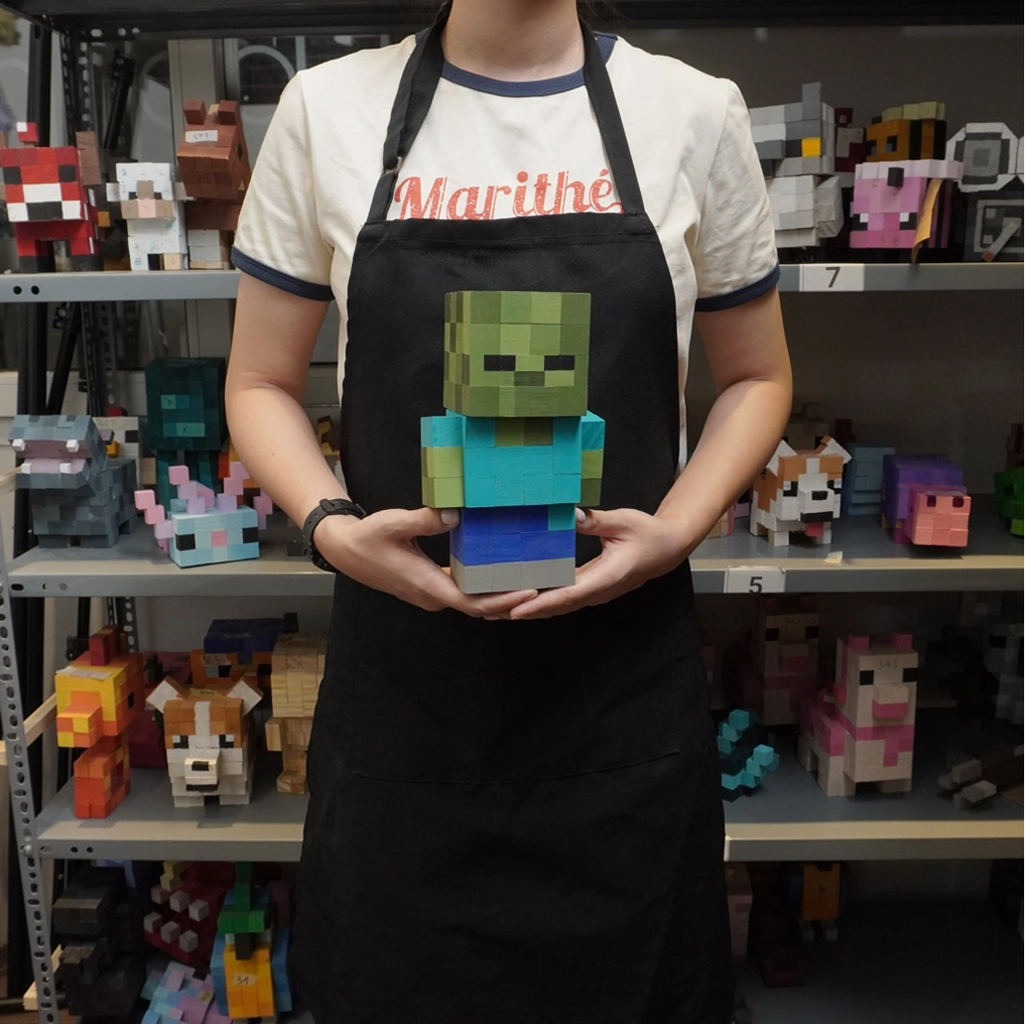 Pixel style wooden zombie figure held by person in apron, handmade toy display