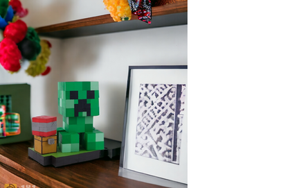 Wooden Minecraft Creeper collectible displayed on wooden shelf beside picture frame.