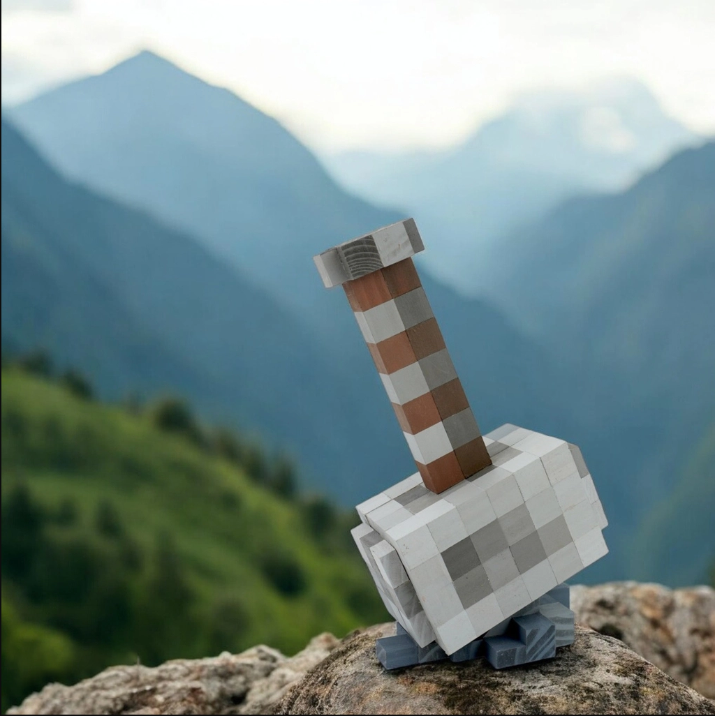 Handmade pixel-style wooden Mjolnir hammer displayed on rock with mountain background.