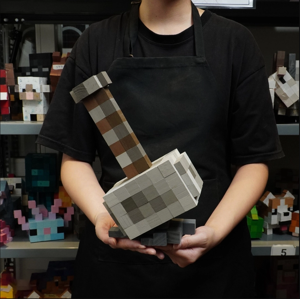 Artisan in black apron holding large handmade Minecraft Mjolnir wooden model.